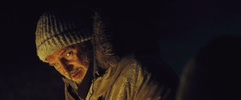 Movie still from “The Grey” (2011), directed by Joe Carnahan – A man in a fur coat and a hat is standing in the dark; Close Up shot, Low angle
