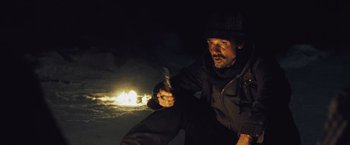 Movie still from “The Grey” (2011), directed by Joe Carnahan – A man sitting on the ground in front of a fire at night; Medium shot, High angle