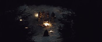 Movie still from “The Grey” (2011), directed by Joe Carnahan – A group of people standing around a fire in the snow; Extreme Wide shot, High angle
