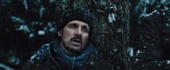 Movie still from “The Grey” (2011), directed by Joe Carnahan – A man in a black hat and jacket standing next to a tree; Close Up shot, Low angle