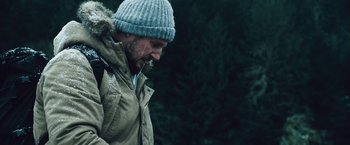 Movie still from “The Grey” (2011), directed by Joe Carnahan – A man in a hat and jacket is standing in the snow; Medium shot, Low angle