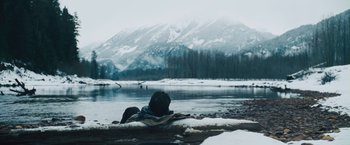 Movie still from “The Grey” (2011), directed by Joe Carnahan – A person sitting on a log near a body of water; Wide shot, Low angle