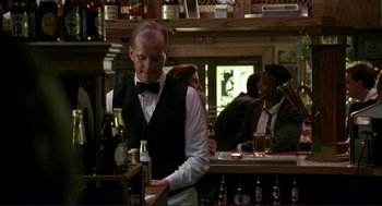 Movie still from “The Grifters” (1990), directed by Stephen Frears – A man standing at a bar pouring a beer; Medium shot, Over the shoulder angle