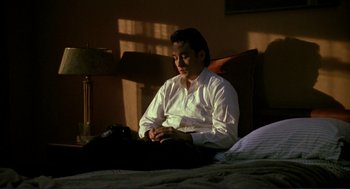 Movie still from “The Grifters” (1990), directed by Stephen Frears – A man sitting on a bed looking at his cell phone; Medium shot, Low angle