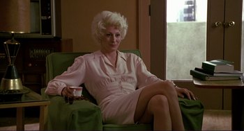 Movie still from “The Grifters” (1990), directed by Stephen Frears – A woman sitting on a green couch holding a remote control; Medium shot, High angle