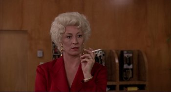 Movie still from “The Grifters” (1990), directed by Stephen Frears – An older woman in a red suit smoking a cigarette; Close Up shot, Low angle