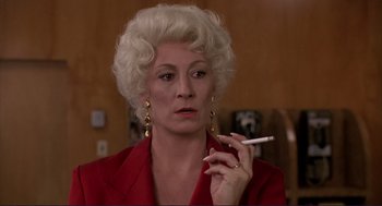 Movie still from “The Grifters” (1990), directed by Stephen Frears – An older woman in a red jacket smoking a cigarette; Close Up shot, Low angle