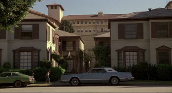 Movie still from “The Grifters” (1990), directed by Stephen Frears – A car parked on the side of the road near a building; Extreme Wide shot, Low angle