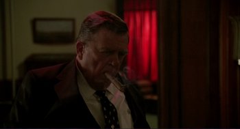 Movie still from “The Grifters” (1990), directed by Stephen Frears – A person wearing a suit smoking a cigarette; Medium shot, Low angle