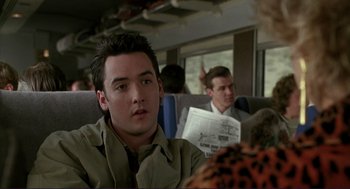 Movie still from “The Grifters” (1990), directed by Stephen Frears – A man sitting on a train holding a newspaper; Medium shot, Over the shoulder angle