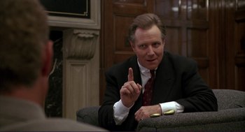 Movie still from “The Grifters” (1990), directed by Stephen Frears – A man in a suit and tie sitting in front of a wall; Close Up shot, Over the shoulder angle