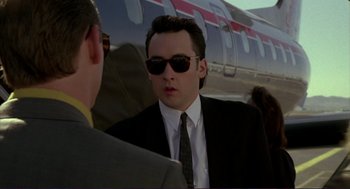 Movie still from “The Grifters” (1990), directed by Stephen Frears – A man in a suit and sunglasses standing in front of an airplane; Close Up shot, Low angle