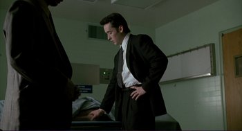 Movie still from “The Grifters” (1990), directed by Stephen Frears – A man in a suit and tie standing next to a bed; Medium shot, Low angle