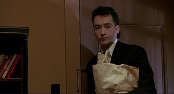 Movie still from “The Grifters” (1990), directed by Stephen Frears – A man in a suit holding a paper bag; Medium shot, Low angle