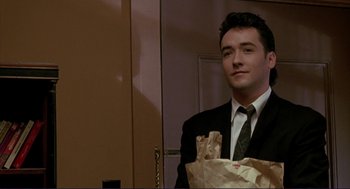 Movie still from “The Grifters” (1990), directed by Stephen Frears – A man in a suit and tie holding a bag of food; Medium shot, Low angle