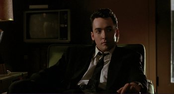 Movie still from “The Grifters” (1990), directed by Stephen Frears – A man in a suit and tie sitting on a couch; Medium shot, Low angle