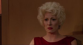 Movie still from “The Grifters” (1990), directed by Stephen Frears – An older woman in a red dress with blonde curly hair; Close Up shot, Over the shoulder angle
