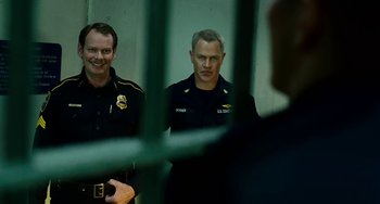 Movie still from “The Guardian” (2006), directed by Andrew Davis – Two police officers standing next to each other in a jail cell; Medium shot, Over the shoulder angle