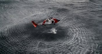 Movie still from “The Guardian” (2006), directed by Andrew Davis – A red and white helicopter flying over a body of water; Extreme Wide shot, Overhead angle