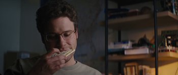 Movie still from “The Guilt Trip” (2012), directed by Anne Fletcher – A man eating a hot dog in a room; Close Up shot, Over the shoulder angle