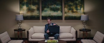 Movie still from “The Guilt Trip” (2012), directed by Anne Fletcher – A man sitting on top of a couch holding a briefcase; Wide shot, Over the shoulder angle