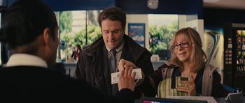 Movie still from “The Guilt Trip” (2012), directed by Anne Fletcher – A man holding a business card in front of a woman; Medium shot, Over the shoulder angle
