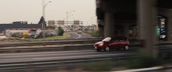 Movie still from “The Guilt Trip” (2012), directed by Anne Fletcher – A red car driving down a street next to an overpass; Extreme Wide shot, High angle