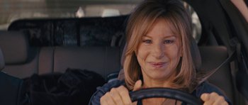 Movie still from “The Guilt Trip” (2012), directed by Anne Fletcher – A woman sitting in the back seat of a car holding a steering wheel; Close Up shot, Over the shoulder angle