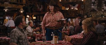 Movie still from “The Guilt Trip” (2012), directed by Anne Fletcher – A woman wearing a cowboy hat standing in front of a table; Medium shot, Over the shoulder angle