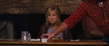 Movie still from “The Guilt Trip” (2012), directed by Anne Fletcher – A woman sitting at a wooden table with a bowl of food in front of her; Medium shot, Over the shoulder angle
