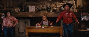 Movie still from “The Guilt Trip” (2012), directed by Anne Fletcher – A woman sitting at a wooden table in front of a fireplace; Medium shot, Over the shoulder angle