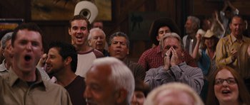 Movie still from “The Guilt Trip” (2012), directed by Anne Fletcher – A group of people in a room with one man talking on a phone; Medium shot, Over the shoulder angle