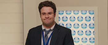 Movie still from “The Guilt Trip” (2012), directed by Anne Fletcher – A man in a suit and tie standing in front of an hsn sign; Close Up shot, Over the shoulder angle