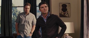 Movie still from “The Guilt Trip” (2012), directed by Anne Fletcher – Two men standing next to each other in a living room; Medium shot, Over the shoulder angle