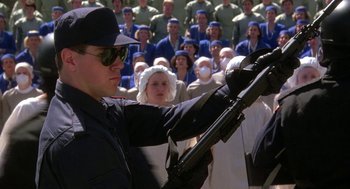 Movie still from “The Handmaid's Tale” (1990), directed by Volker Schlöndorff – A man holding a gun in front of a crowd of people; Medium shot, Over the shoulder angle
