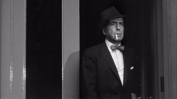 Movie still from “The Harder They Fall” (1956), directed by Mark Robson – A black and white photo of a man smoking a cigarette; Medium shot, Low angle