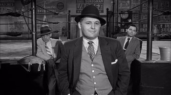 Movie still from “The Harder They Fall” (1956), directed by Mark Robson – A black and white photo of a man in a suit and hat; Medium shot, Low angle