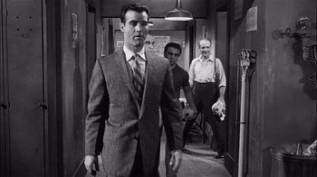 Movie still from “The Harder They Fall” (1956), directed by Mark Robson – A man in a suit walking down a hall way; Medium shot, Over the shoulder angle