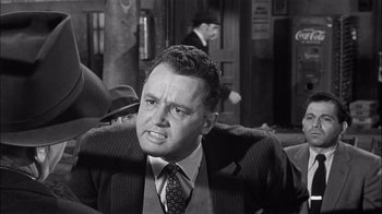 Movie still from “The Harder They Fall” (1956), directed by Mark Robson – An old black and white photo of a man in a suit; Close Up shot, Over the shoulder angle