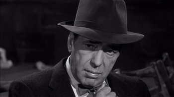 Movie still from “The Harder They Fall” (1956), directed by Mark Robson – A man in a suit and tie wearing a hat; Close Up shot, Over the shoulder angle