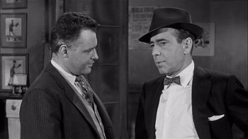 Movie still from “The Harder They Fall” (1956), directed by Mark Robson – A black and white photo of two men in suits; Medium shot, Low angle