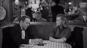 Movie still from “The Harder They Fall” (1956), directed by Mark Robson – A man and a woman sitting at a table in a restaurant; Medium shot, Over the shoulder angle