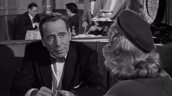 Movie still from “The Harder They Fall” (1956), directed by Mark Robson – A man and a woman sitting at a table in a restaurant; Close Up shot, Over the shoulder angle