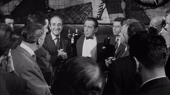 Movie still from “The Harder They Fall” (1956), directed by Mark Robson – A black and white photo of a group of men in tuxedos; Medium shot, Over the shoulder angle