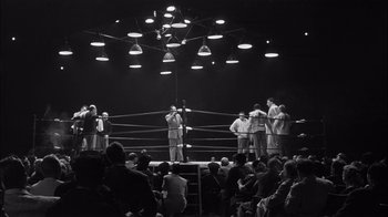 Movie still from “The Harder They Fall” (1956), directed by Mark Robson – A group of men standing on top of a boxing ring; Extreme Wide shot, Low angle