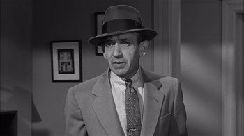 Movie still from “The Harder They Fall” (1956), directed by Mark Robson – A man wearing a suit and a hat in black and white; Close Up shot, High angle