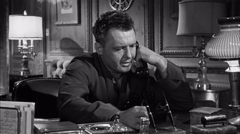Movie still from “The Harder They Fall” (1956), directed by Mark Robson – A man sitting at a table talking on a phone; Close Up shot, High angle