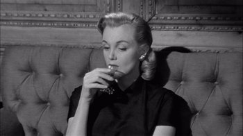 Movie still from “The Harder They Fall” (1956), directed by Mark Robson – A woman sitting on a couch holding a glass of wine; Close Up shot, Low angle