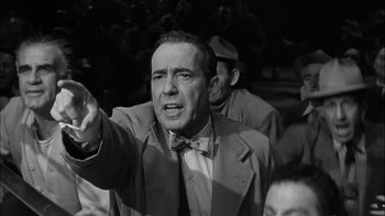 Movie still from “The Harder They Fall” (1956), directed by Mark Robson – An old photo of a man in a suit and a bow tie; Medium shot, Low angle