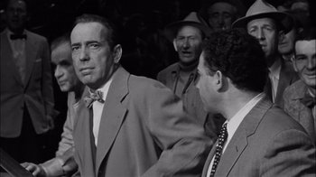 Movie still from “The Harder They Fall” (1956), directed by Mark Robson – A black - and - white photo of two men in suits; Medium shot, Over the shoulder angle
